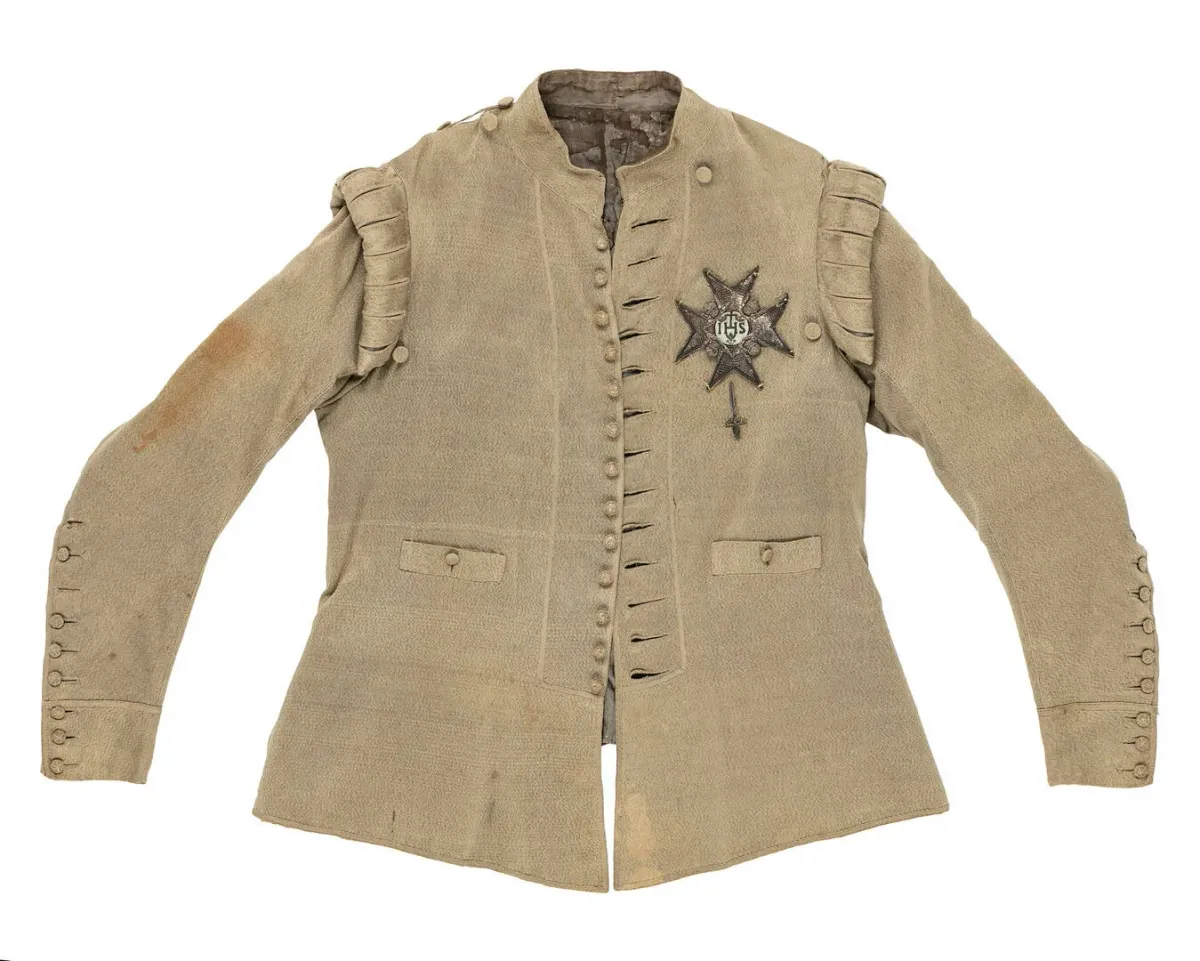 Veste brun clair sur fond blanc, vue de face, avec manches, boutons et insigne brodé sur la poitrine.