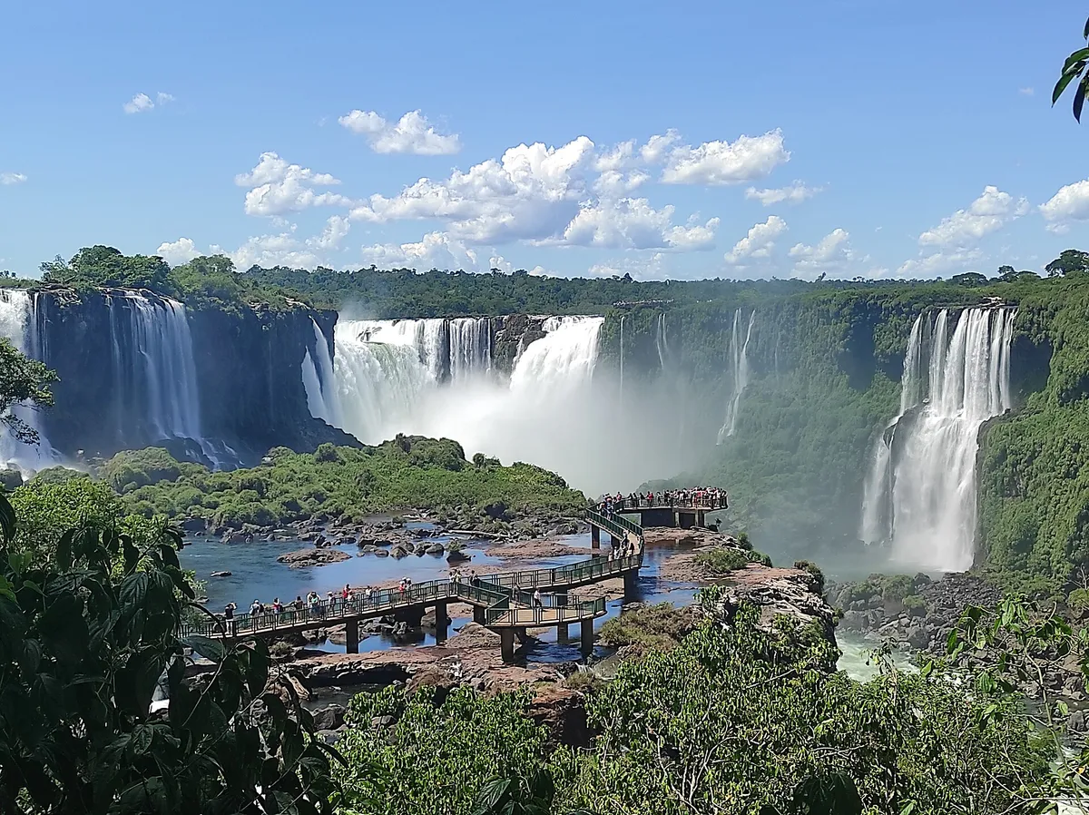 Quedas largas sobre um cânion verde, com uma passarela junto à água.