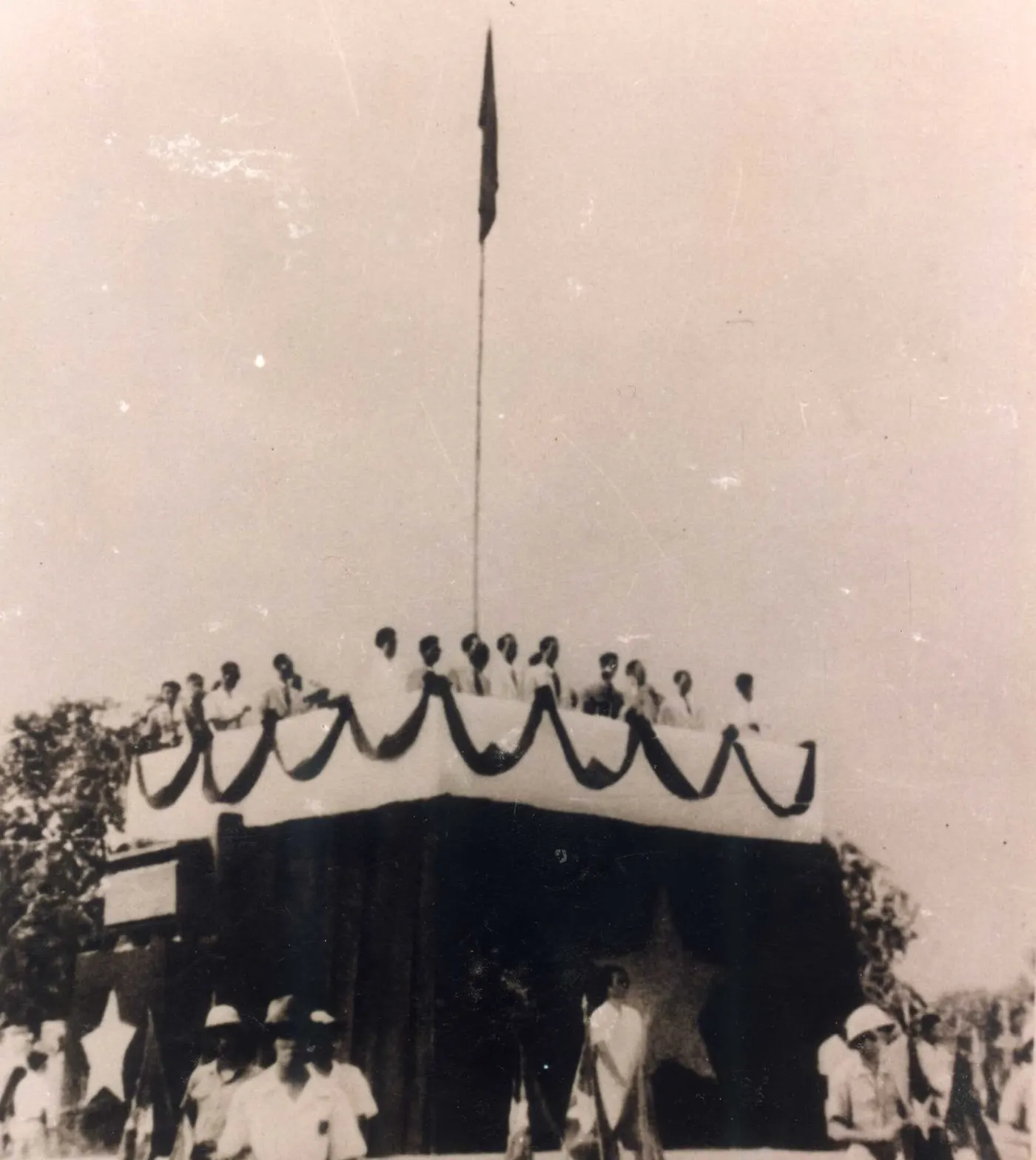 Um palanque com uma bandeira no mastro e pessoas pequenas em cima e embaixo.
