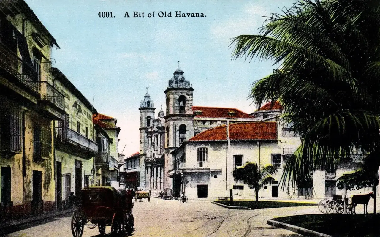 Cartão-postal colorido mostra uma rua de Havana Velha, com as torres da catedral ao fundo, prédios coloniais com sacadas, uma carruagem puxada por cavalos e uma palmeira.