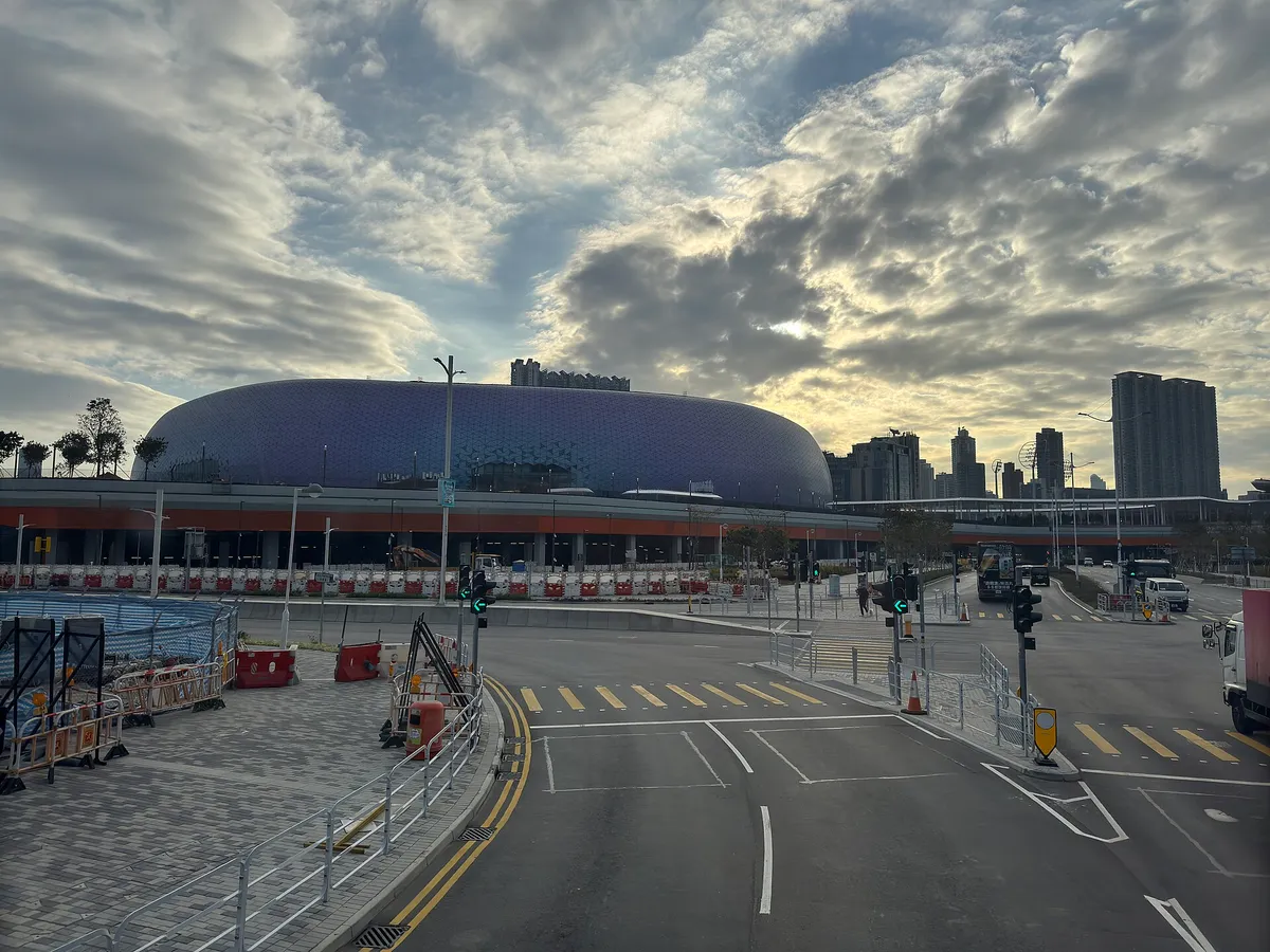 Um estádio de cúpula roxa, visto de uma avenida, com barreiras de obra na frente.