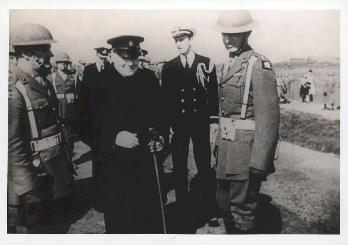 Fotografia em preto e branco de Churchill com oficiais e soldados uniformizados, dentro da margem branca do original.