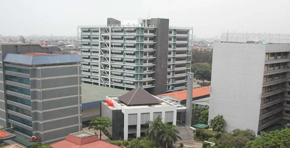 Prédios de um campus com uma torre central, um telhado em pirâmide e palmeiras.