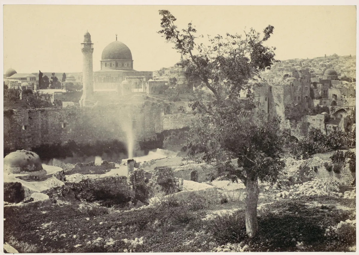 Fotografia antiga com a cúpula à esquerda, uma árvore no centro e ruínas e edifícios de pedra ao redor.