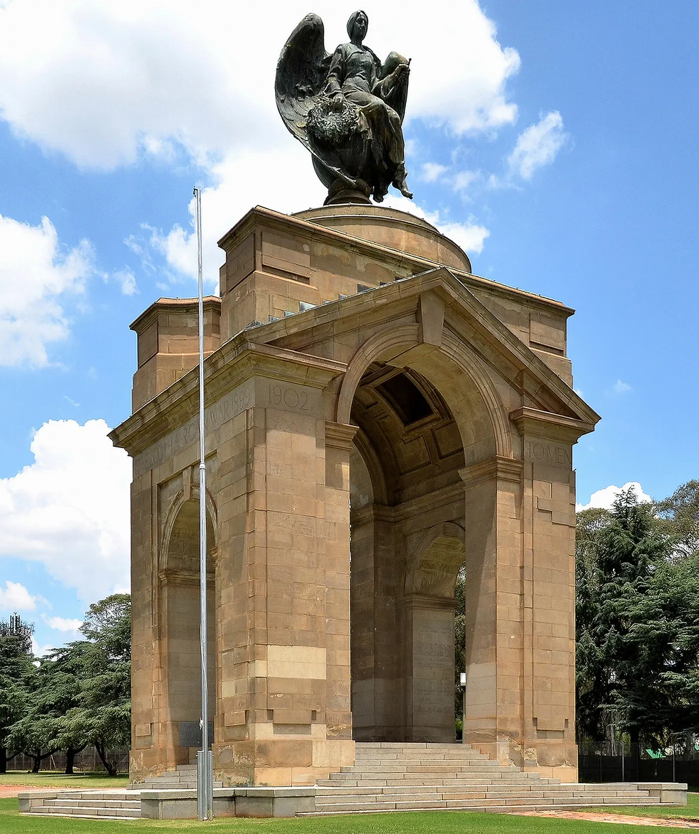 Um arco de pedra com uma figura de bronze alada no topo, sem pessoas.