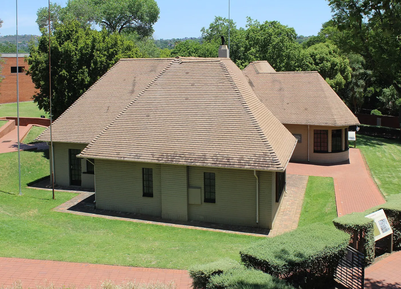 Uma casa baixa de telhado marrom, com um volume redondo ao lado, no meio de um gramado.