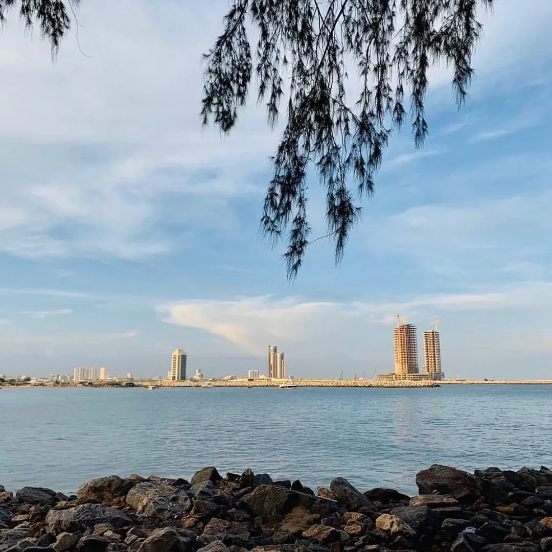 New towers across the water, with a breakwater and rocks in the foreground.
