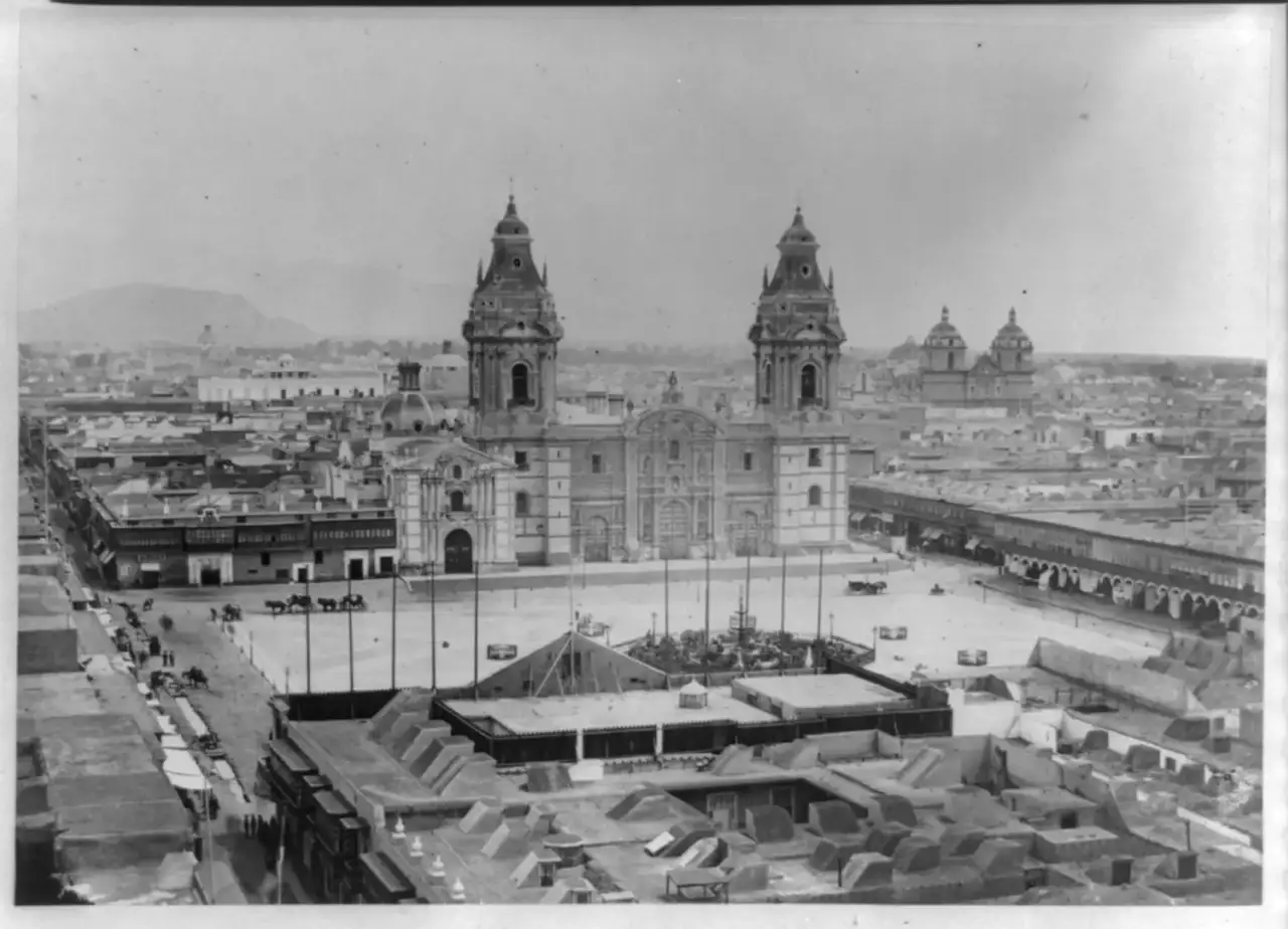 Fotografia aérea em preto e branco da Plaza Mayor de Lima, com a catedral de duas torres ao fundo e um mercado coberto em primeiro plano.