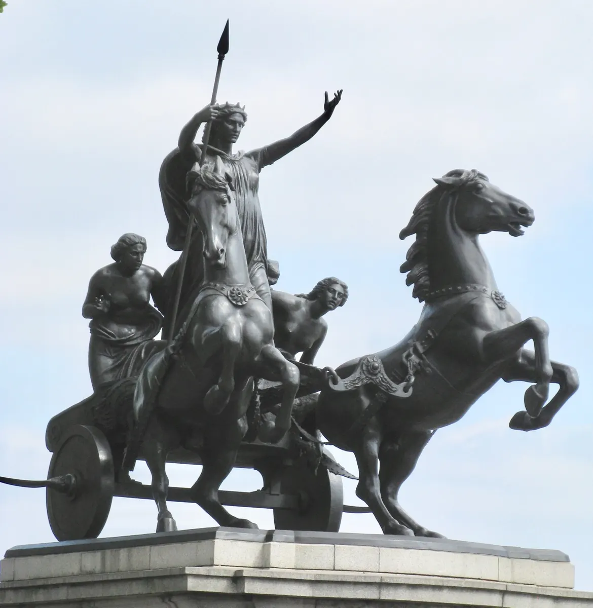 Escultura de bronze de Boudica e duas figuras numa carruagem puxada por cavalos, com lança e braço erguido.