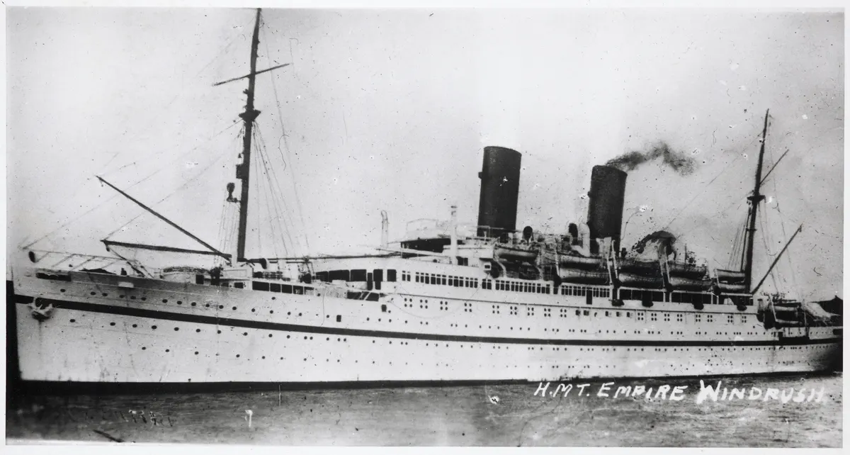 Fotografia do navio Empire Windrush de perfil, com dois funis, mastros e identificação manuscrita na margem branca inferior.