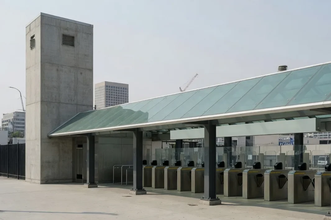 Entrada de estação com cobertura de vidro, colunas de aço e catracas.
