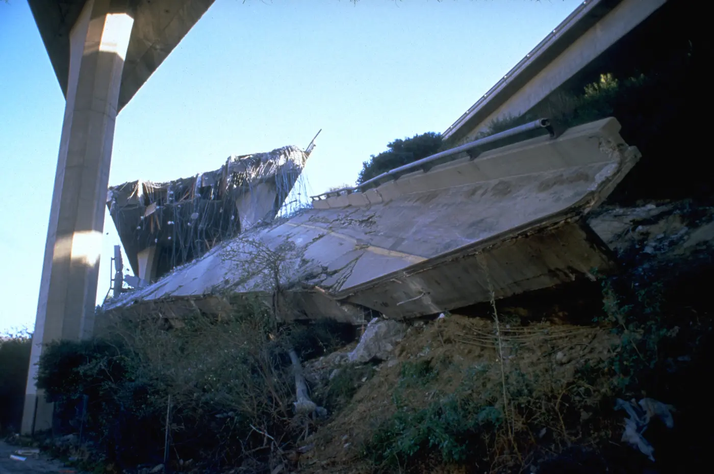 Laje de concreto caída sob o viaduto, com ferragens à mostra e o céu limpo.