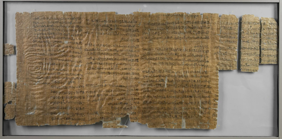 Papiro marrom com linhas de escrita hierática e fragmentos separados, inteiros no enquadramento.