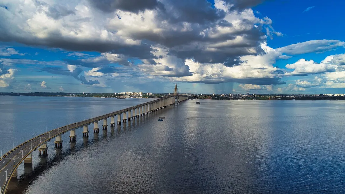 Puente atirantado sobre un río ancho y oscuro, con un mástil en el centro y nubes de lluvia.