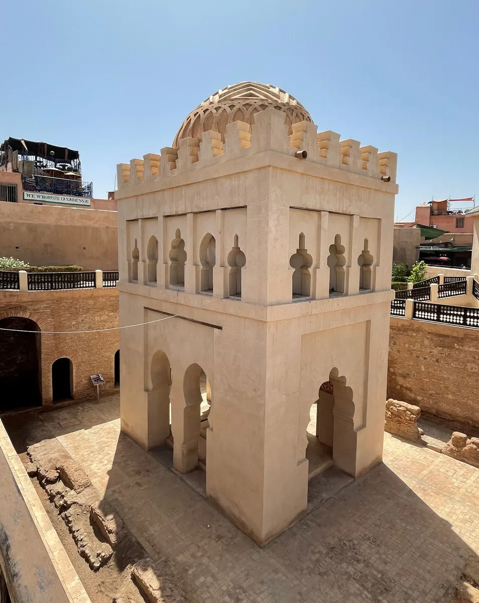Pavilhão de pedra clara com arcos e cúpula nervurada, visto inteiro de cima, entre ruínas e guarda-corpos.