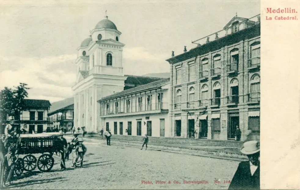 Igreja de torre branca ao lado de um prédio de arcadas, uma carruagem e pessoas na praça.