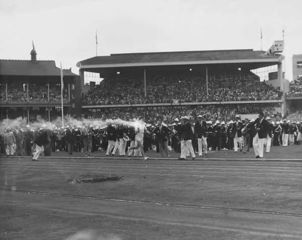 A runner with the torch crosses the grass of a packed stadium.