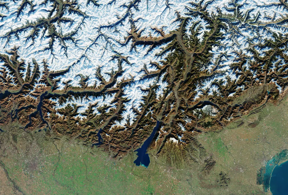 Imagem orbital do norte da Itália e dos Alpes, com montanhas nevadas, lagos e a planície onde fica Milão.