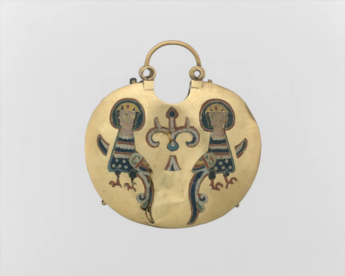 Pendente dourado com grande argola superior, duas pequenas alças e esmalte com duas aves de cabeça humana junto a uma árvore, sobre fundo branco.