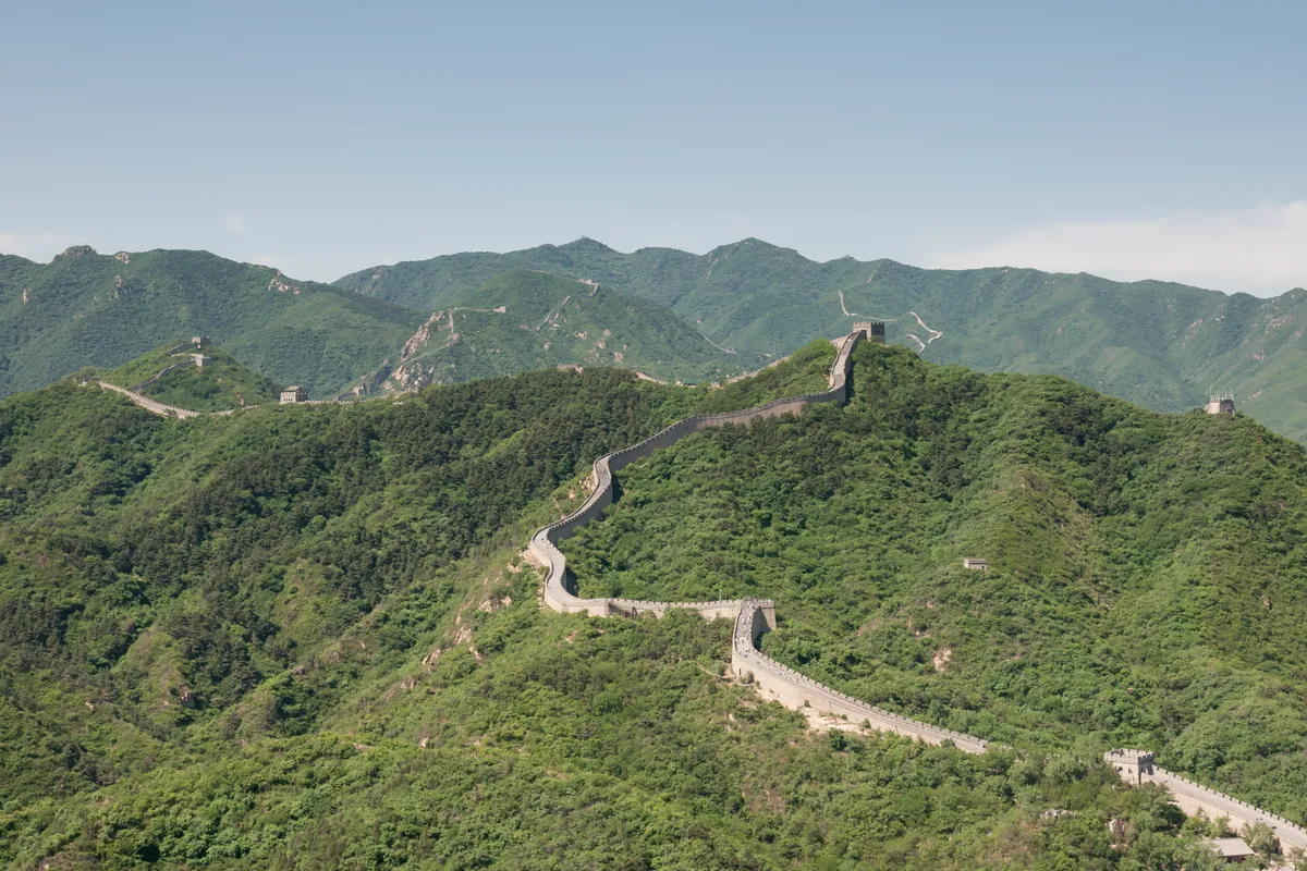 A muralha de pedra serpenteia pelas cristas verdes, com torres de vigia ao longo do traçado.