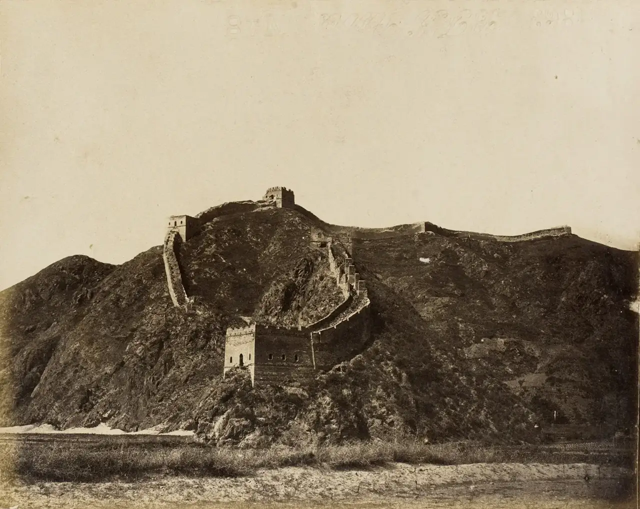 Um trecho murado sobe a crista de uma montanha rochosa e sem vegetação, com duas torres de vigia quadradas, em 1860.