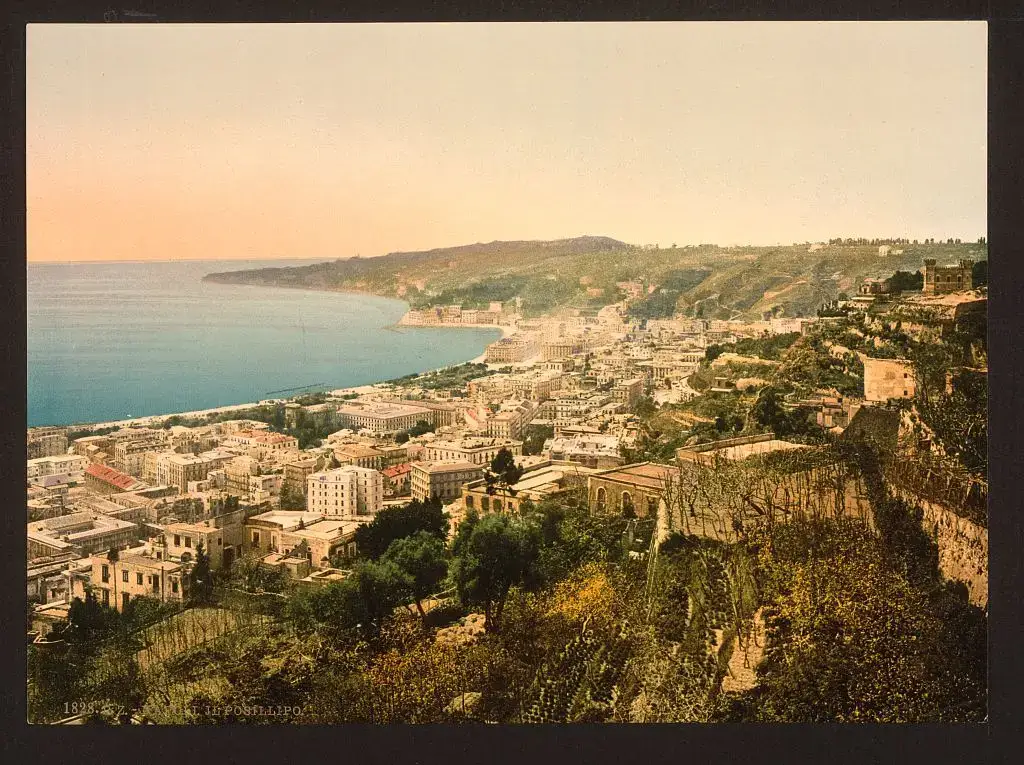 Vista da cidade de Nápoles em curva ao longo da baía, vista de cima da colina do Posillipo, com o mar à esquerda e casas na encosta.
