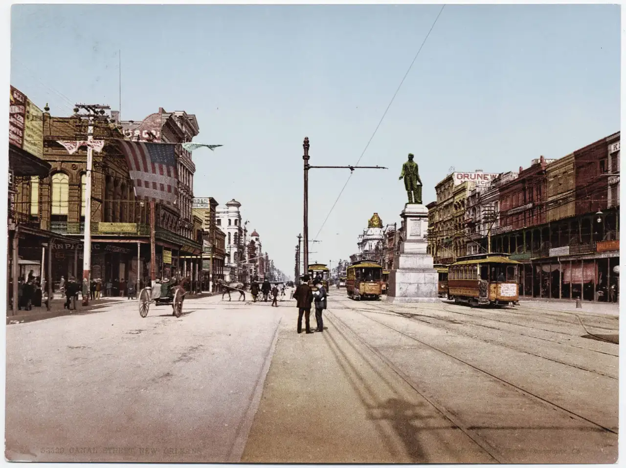 Bondes elétricos e pedestres na Canal Street, ao lado da estátua de Henry Clay e de fachadas comerciais decoradas com bandeiras.