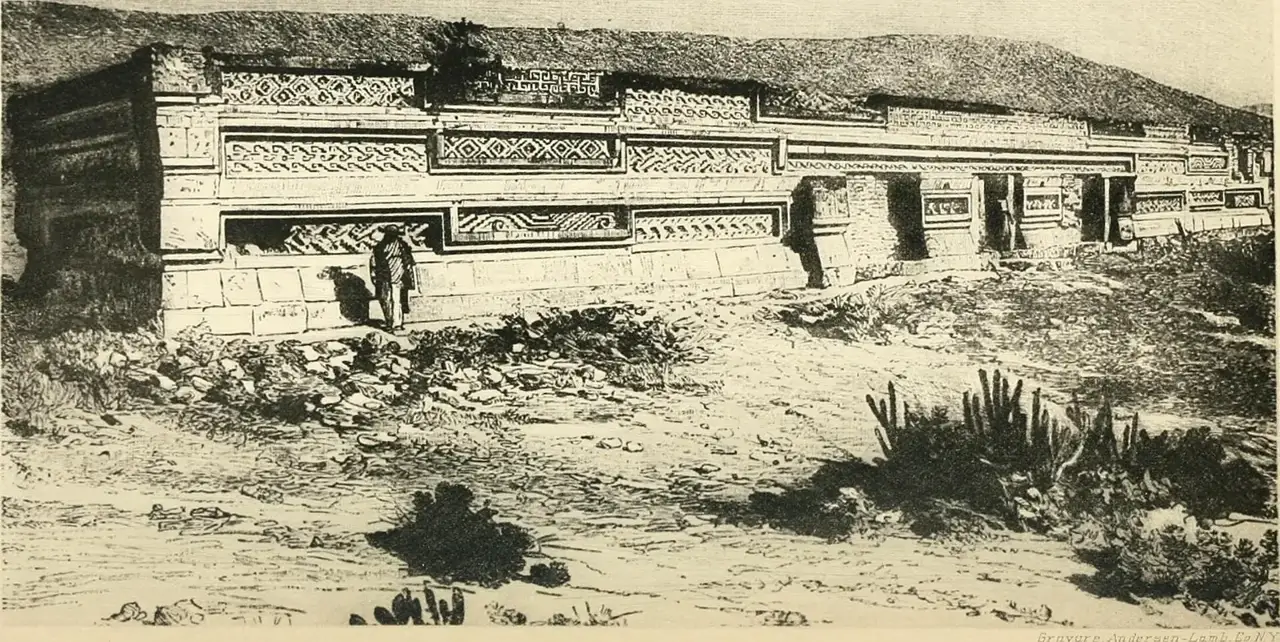 Gravura de uma parede de pedra com mosaicos geométricos entalhados, parte do sítio arqueológico de Mitla, com um homem parado diante dela.