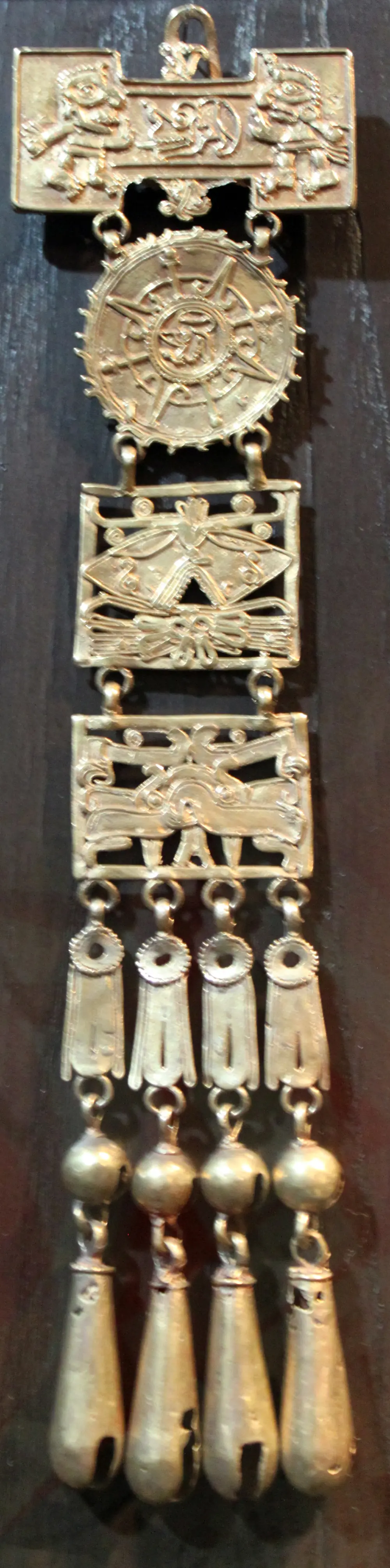 Brinco de ouro comprido, com placas recortadas e pingentes, sobre fundo escuro.