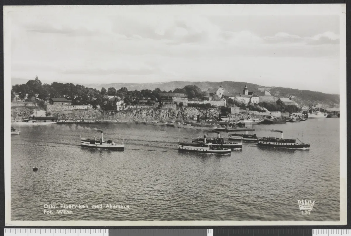 Cartão-postal com barcos diante da fortaleza de Akershus, água em primeiro plano, margens claras e escala de referência inferior.