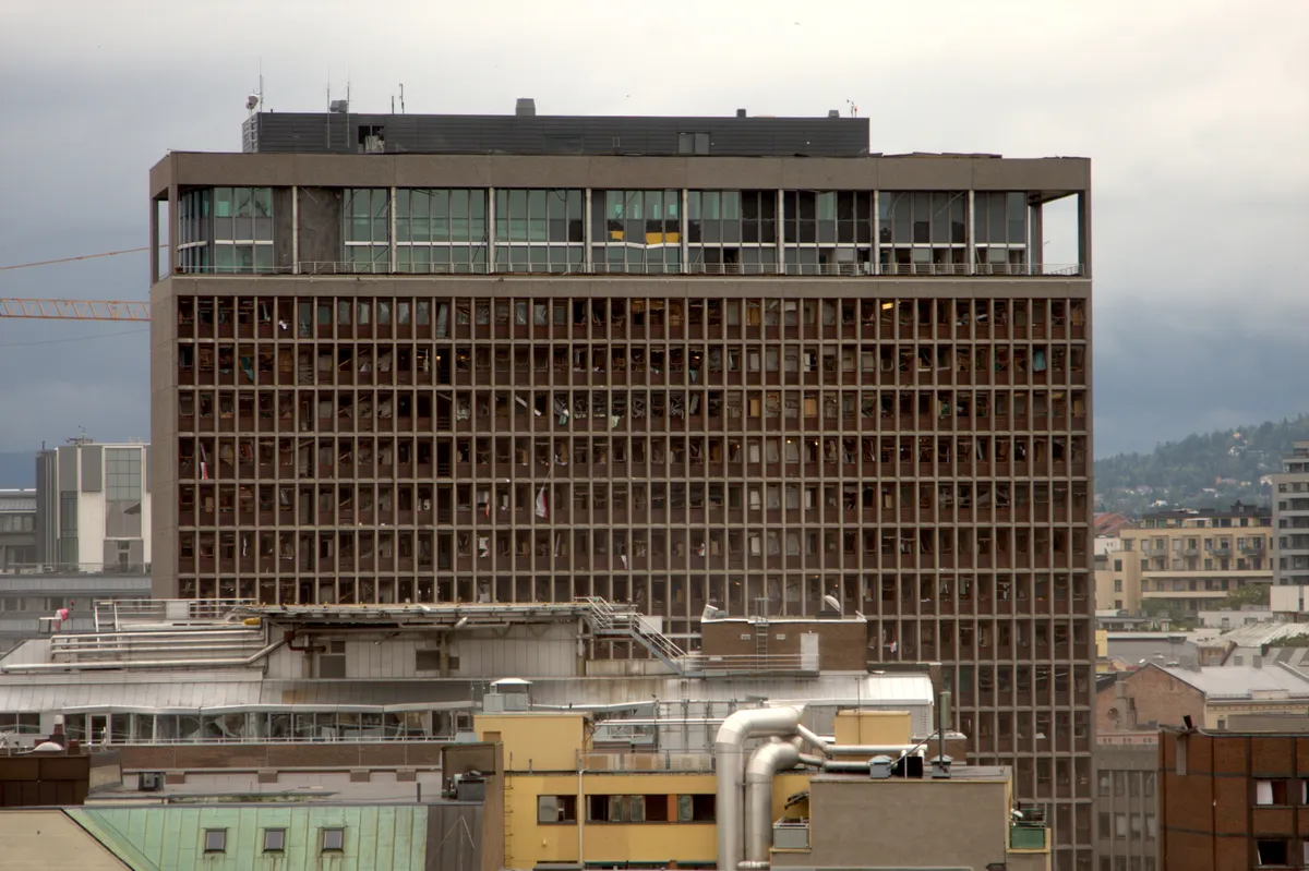 Bâtiment élevé aux rangées de fenêtres brisées et antennes sur le toit, vu au-dessus de toits plus bas.