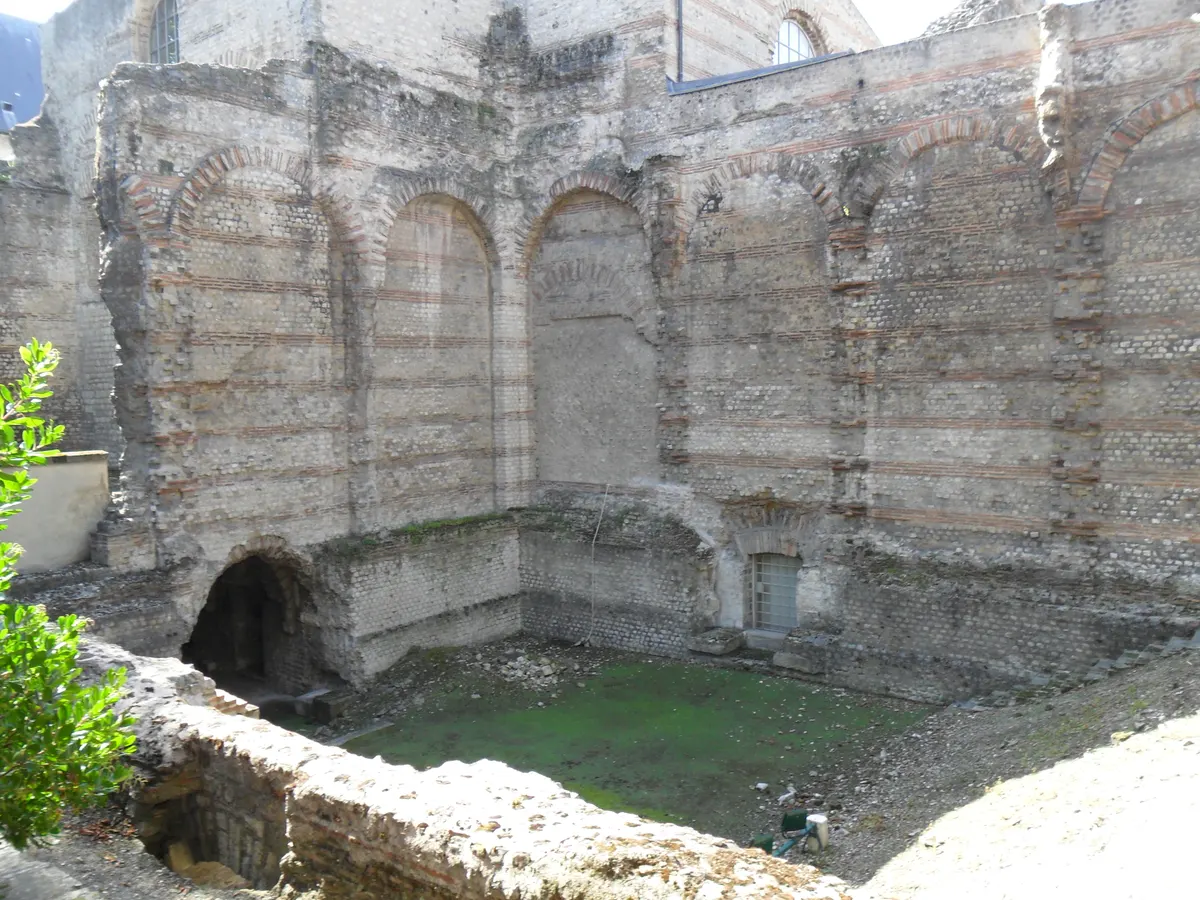 Ruínas das termas de Cluny, com paredes de pedra e tijolo, arcos e vegetação no chão.