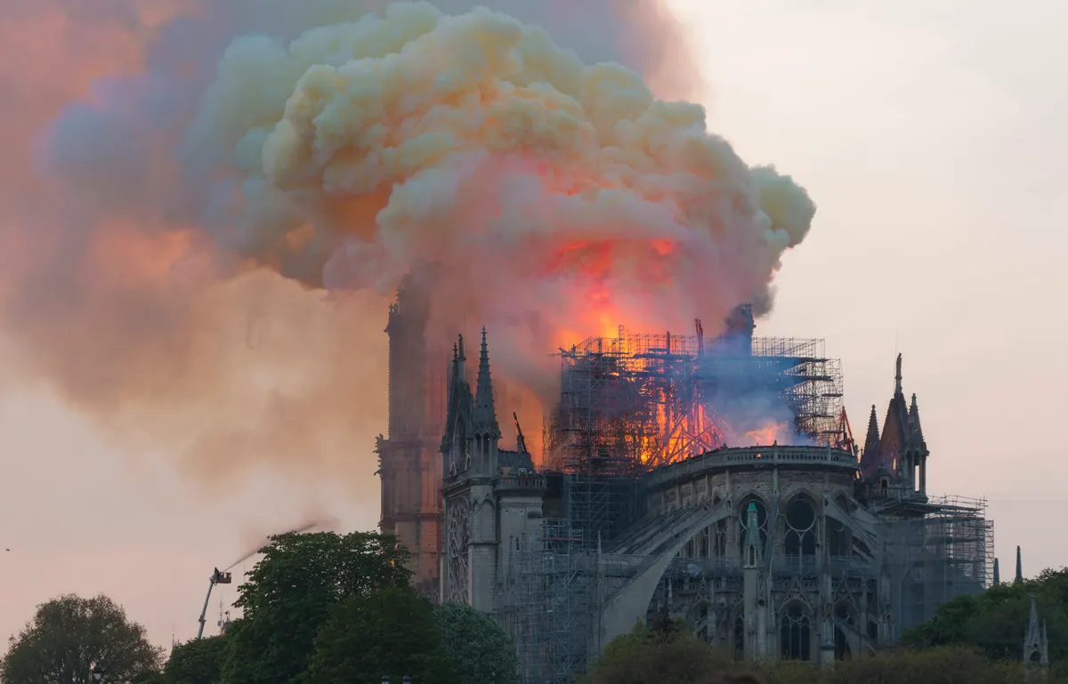 Notre-Dame durante o incêndio, com chamas atrás dos andaimes, fumaça e jatos de água sobre a igreja.