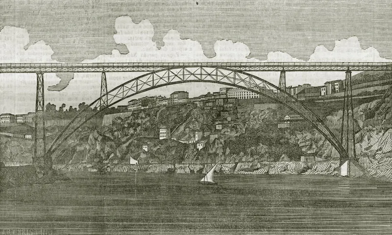 Gravura em preto e branco da ponte Maria Pia, com um grande arco de ferro sobre o Douro, tabuleiro elevado, casas e barcos nas margens.