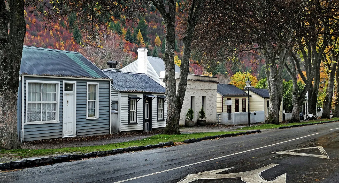 Uma rua vazia de casas baixas de madeira, com árvores de outono e o asfalto molhado.