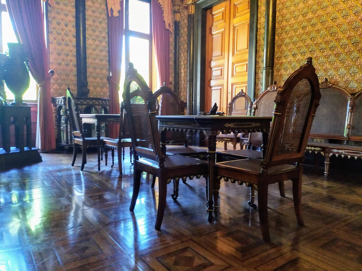 Sala com cadeiras de palhinha, mesa de madeira escura, piso de parquet e parede com padrão repetido.