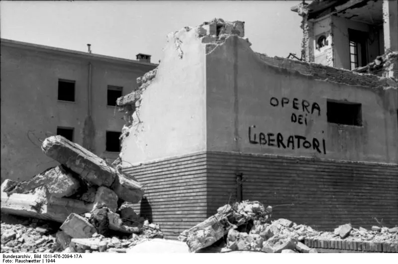 Edifício destruído em Roma, com paredes abertas, escombros e inscrição de propaganda de guerra numa fachada.