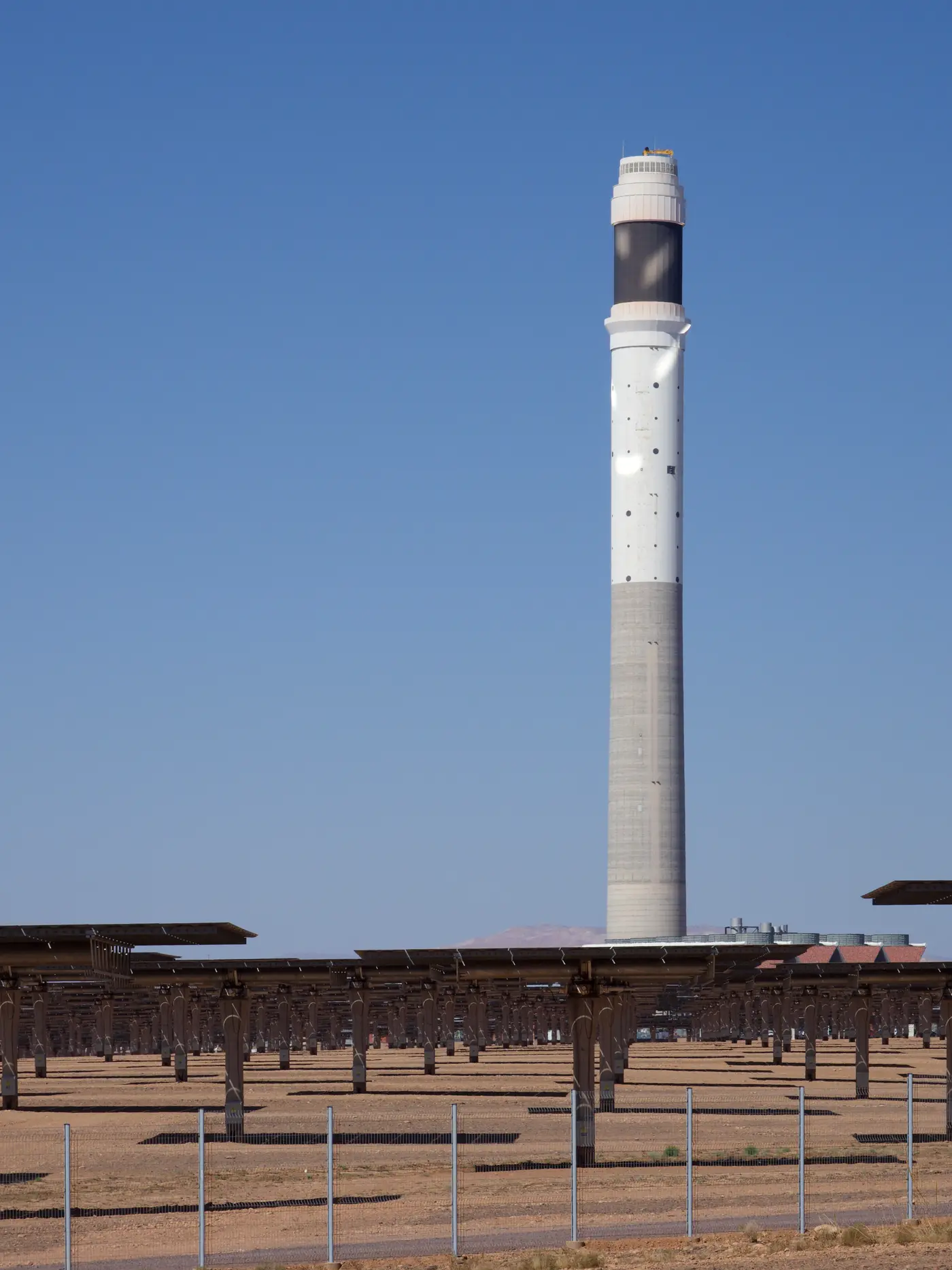 Torre branca e cinza, com uma faixa escura perto do topo, sobre um campo de espelhos no deserto.