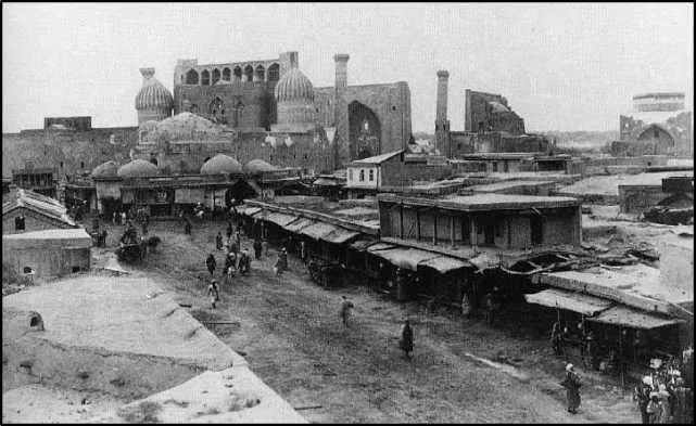 Vista elevada de um bazar de barracas, com gente miúda na rua e, ao fundo, um edifício de cúpulas e um grande arco.