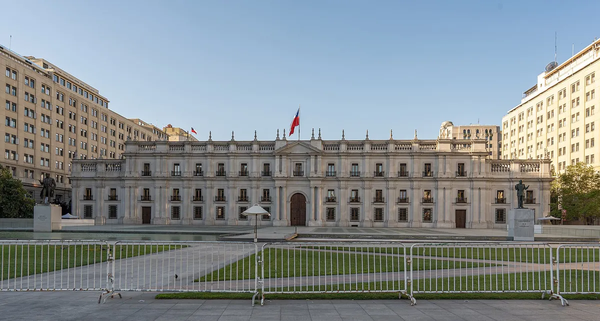 A fachada branca de La Moneda, com a bandeira do Chile e a praça vazia na frente.