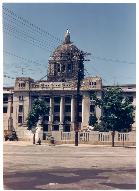 Um edifício de pedra com colunas e uma cúpula em andaime, visto do outro lado de uma avenida.