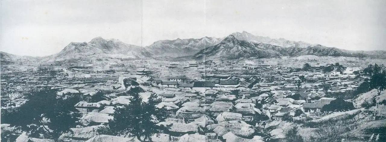 Vista panorâmica de Seul a partir da antiga muralha da cidade, com telhados baixos cobrindo o vale e montanhas ao fundo.