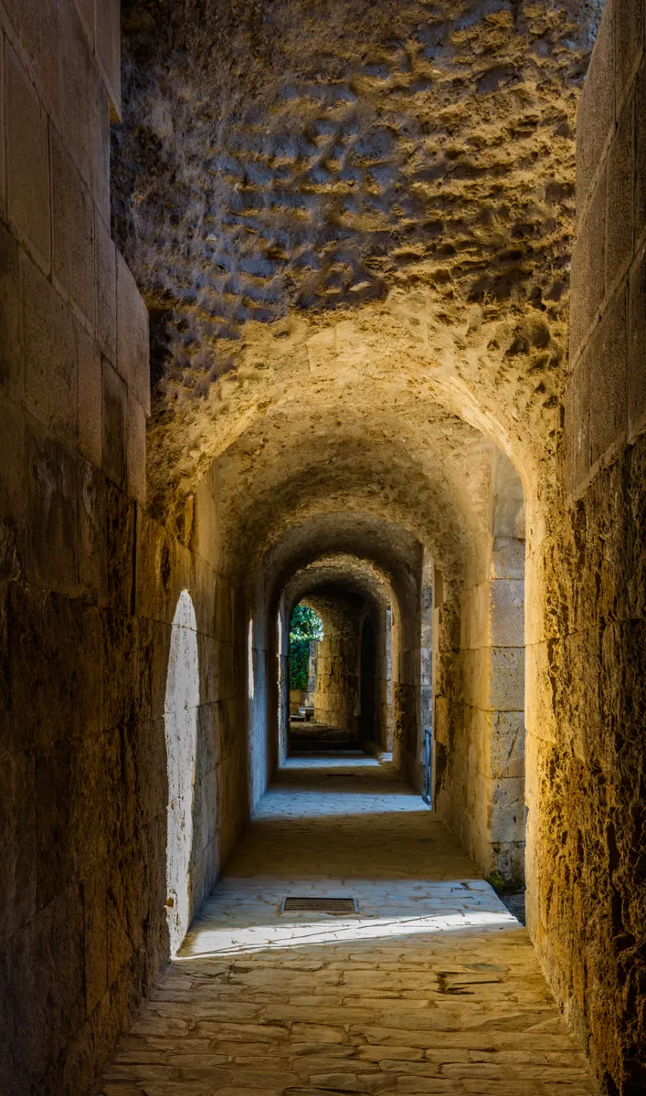 Galeria de alvenaria do anfiteatro de Itálica, com abóbadas sucessivas, aberturas laterais e piso de pedra.