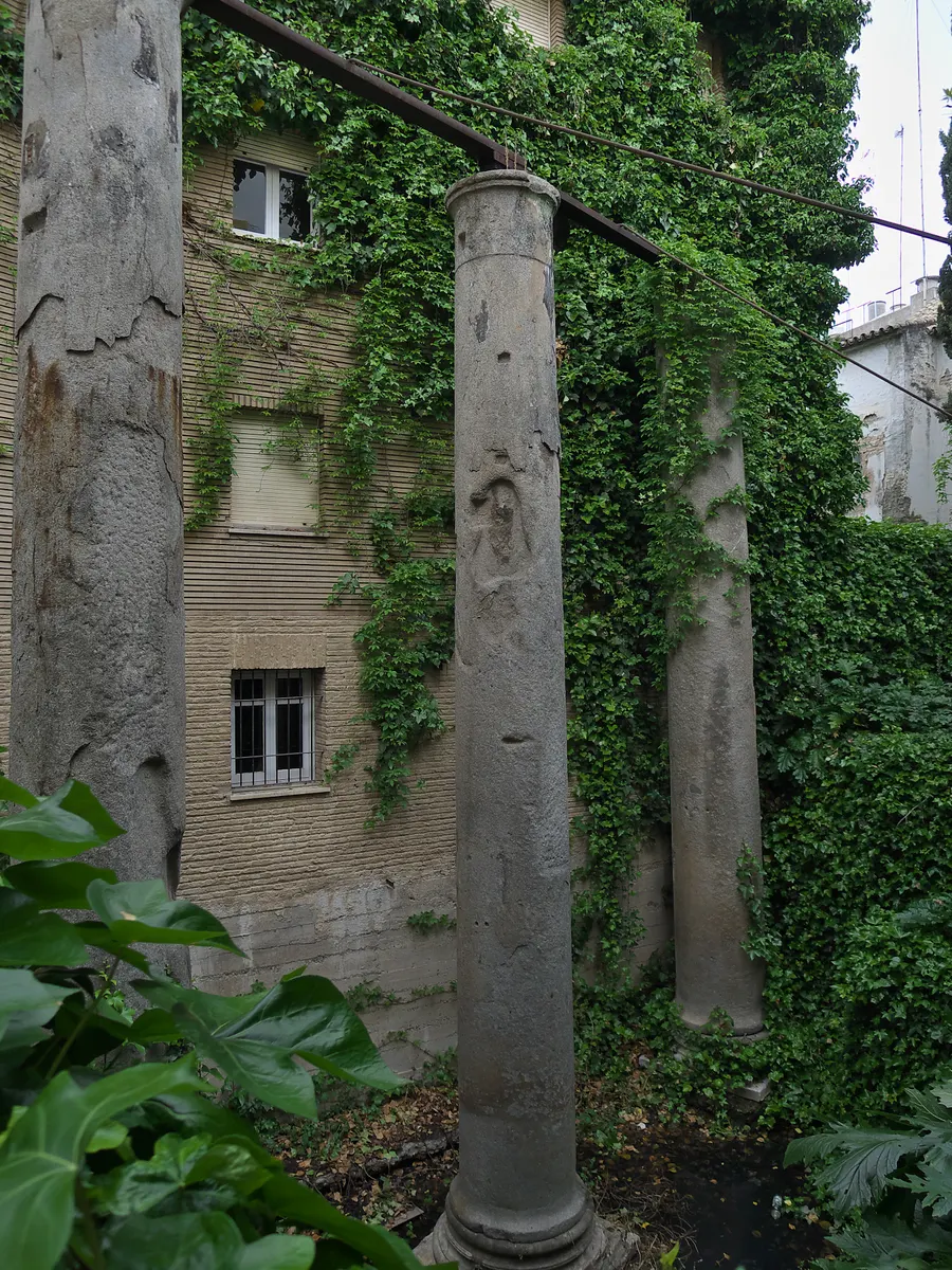 Colunas romanas de granito entre árvores e edifícios da calle Mármoles, em terreno abaixo do nível da rua.