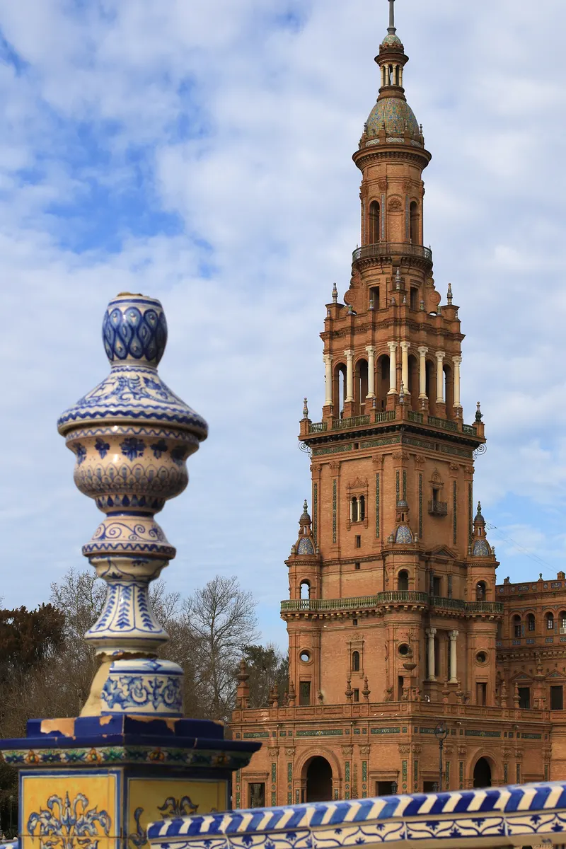Detalhe de torre de tijolos da Plaza de España, atrás de balaustrada e ornamento de cerâmica azul e branca.
