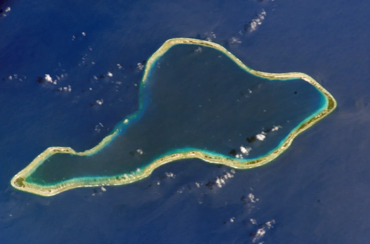 Anel de recife em volta de uma lagoa azul, visto de cima, no oceano.