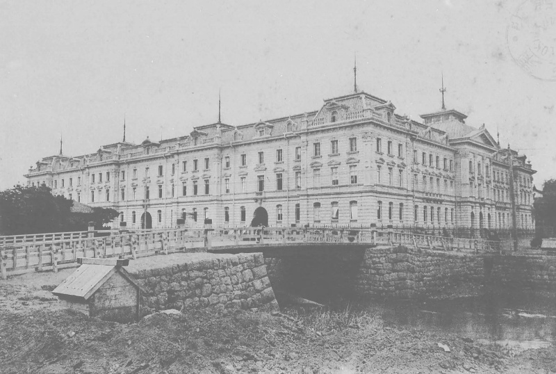 Edifício longo de vários pavimentos, ao lado de uma ponte e margem de pedra.