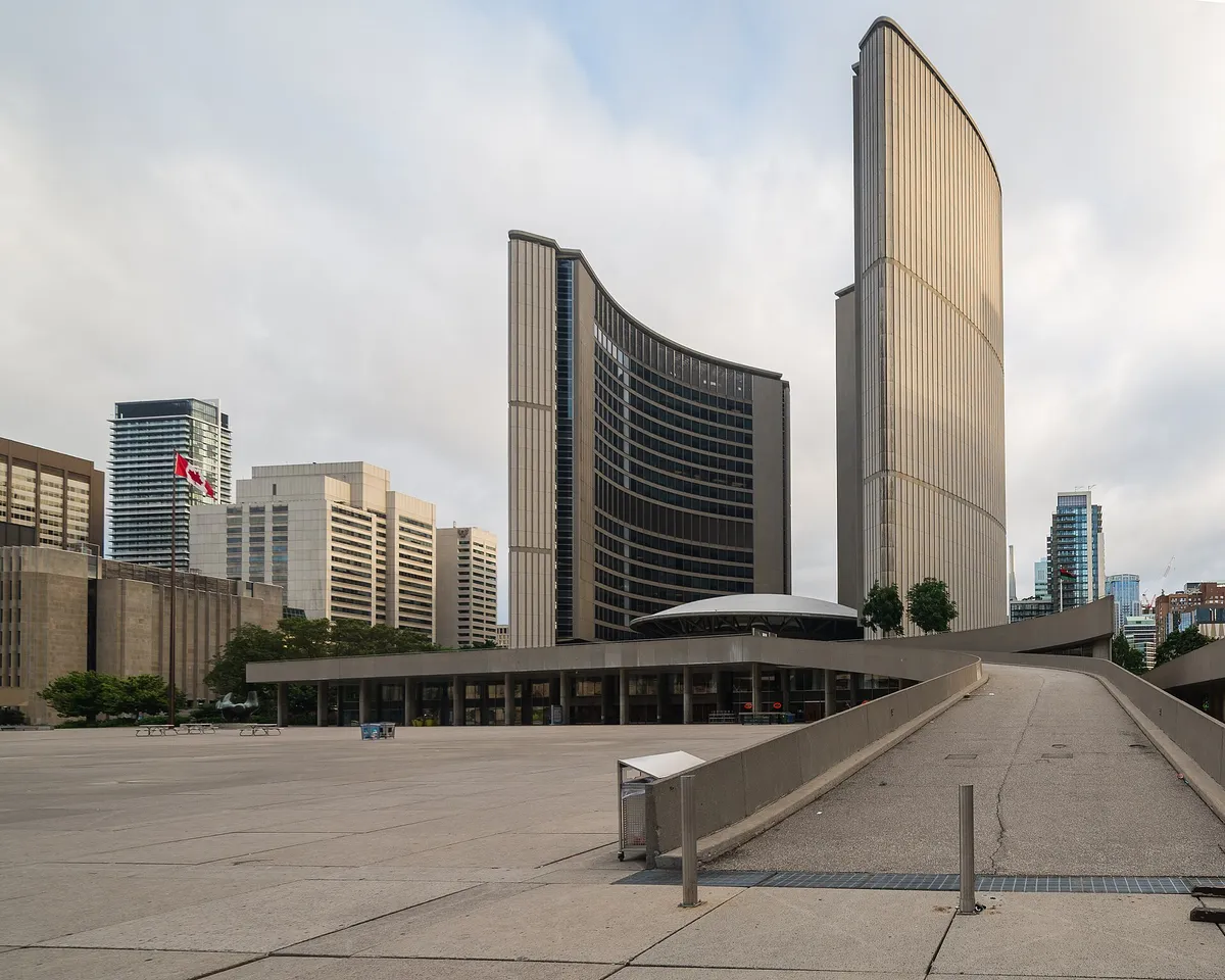 Duas torres curvas sobre uma praça vazia, com a bandeira do Canadá à esquerda.