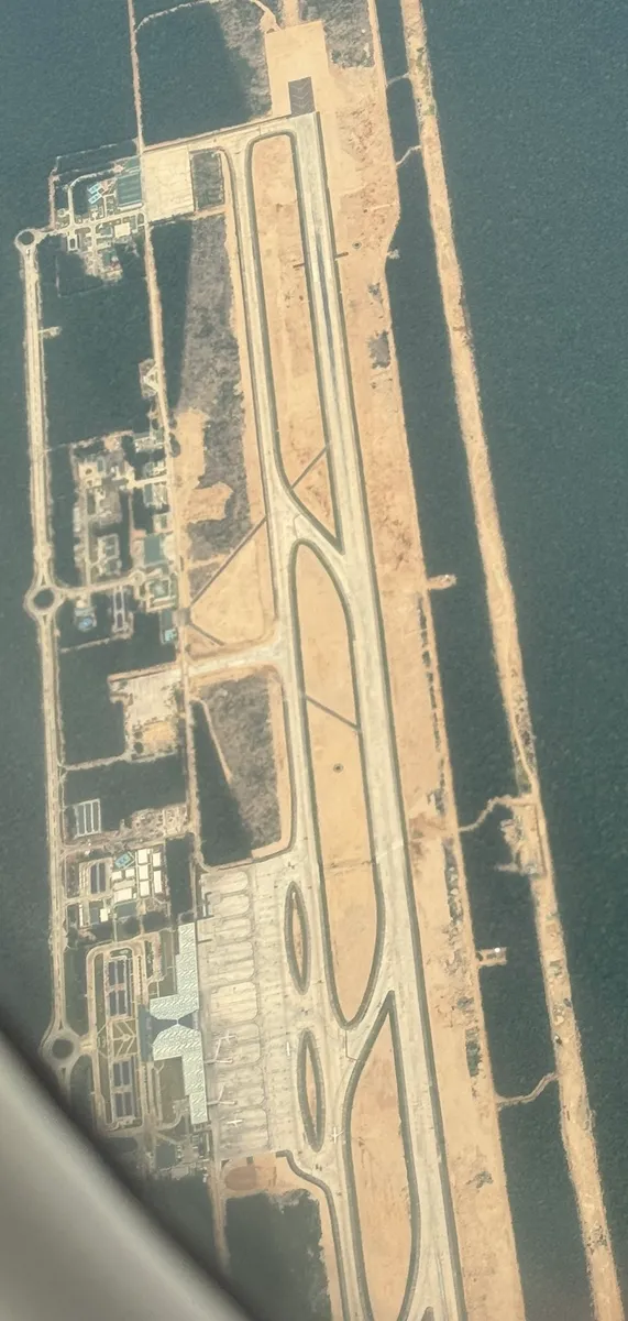 Vista aérea diagonal de parte do aeroporto de Tulum, com pátios, aeronaves, pista e floresta ao redor.