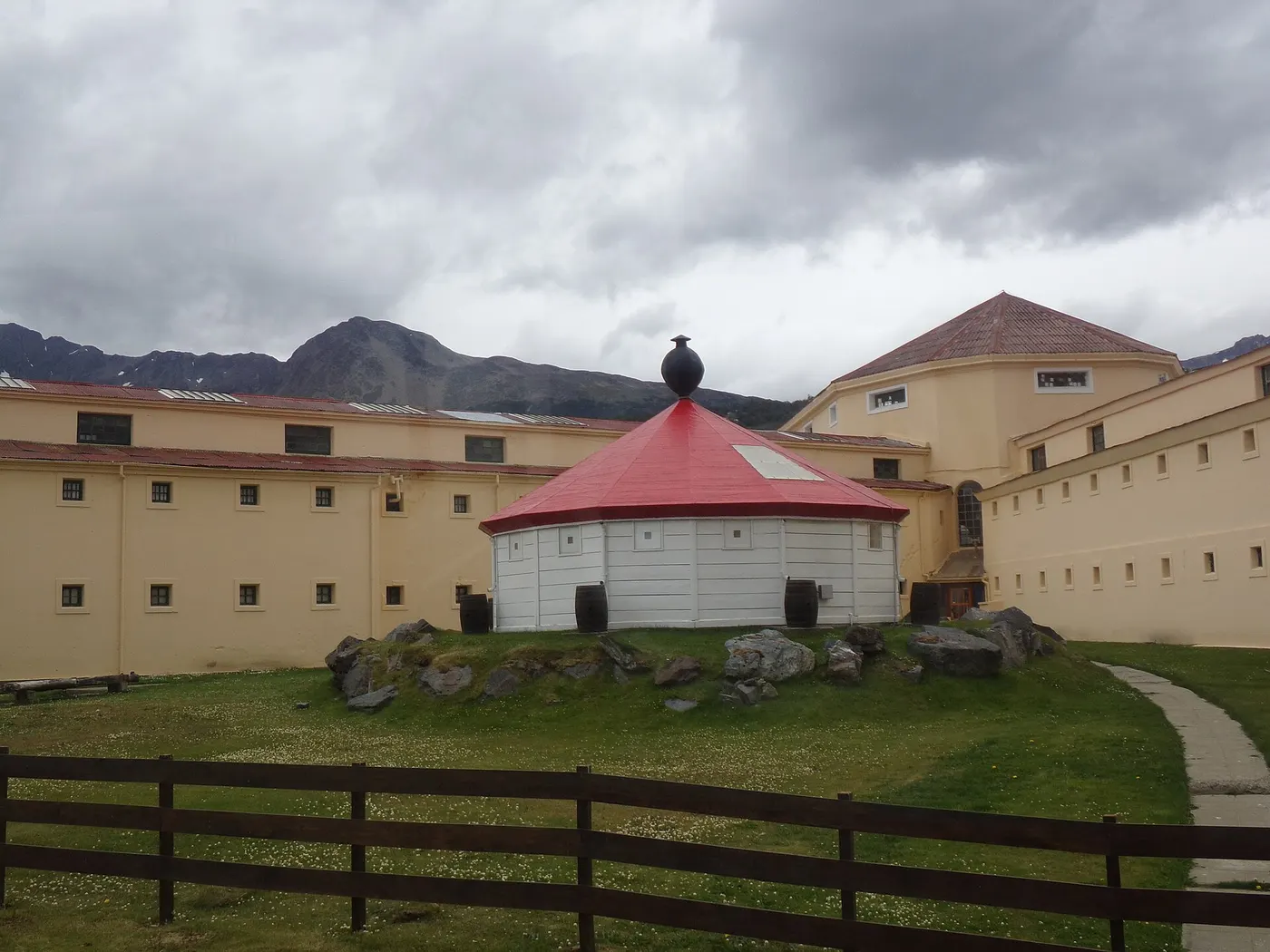 Pavilhões amarelos de janelas pequenas e um telhado vermelho no pátio, com montanhas atrás e sem pessoas.